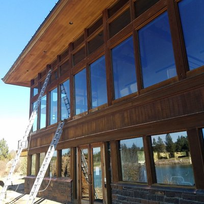 Two-story wood-framed windows on a Central Oregon home with ladders set for exterior cleaning