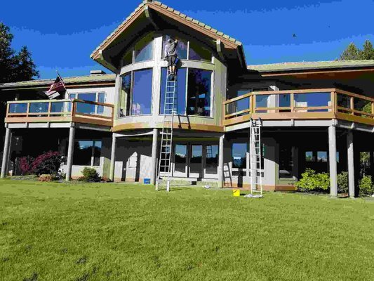 Multi-level Central Oregon home with crew cleaning large upper windows from ladders