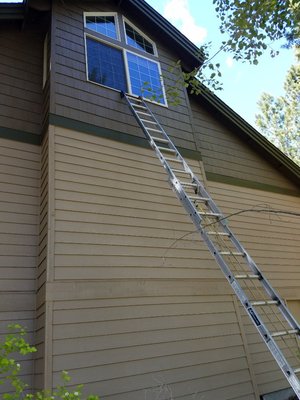 Tall extension ladder reaching a high gable window on a two-story home