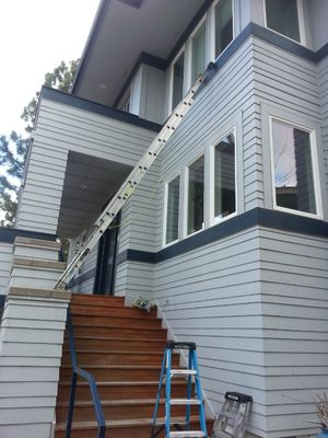 Two-story light blue home with ladders set for multi-level exterior window cleaning