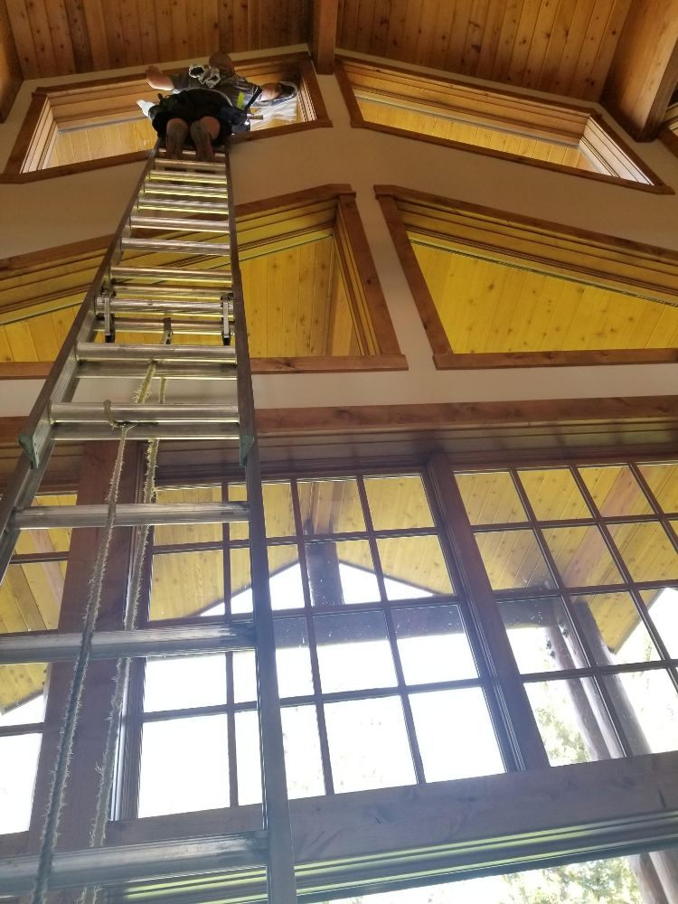 Technician cleaning high vaulted interior windows from a tall ladder